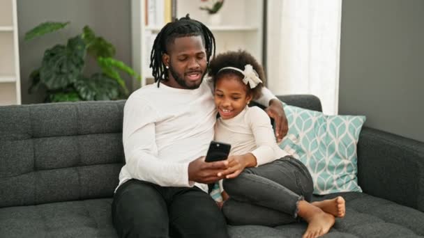 Afrykański Amerykański Ojciec Córka Pomocą Smartfona Siedzi Kanapie Uśmiechnięty Domu — Wideo stockowe