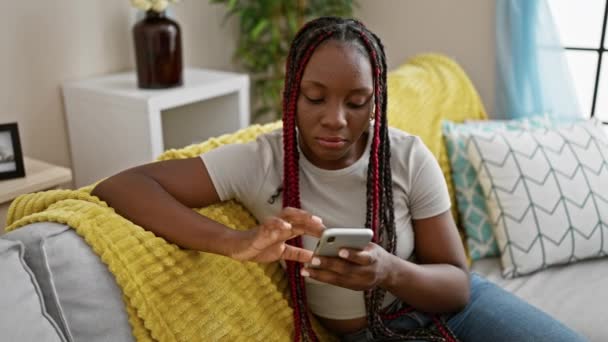 快乐的非洲裔美国女人喜欢用智能手机发短信 的手势表达喜悦 舒服地坐在家里沙发上 — 图库视频影像