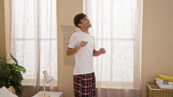 若いヒスパニックの男は喜んで朝に踊り 窓に向かって寝室の毛布を投げる — ストック動画