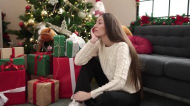 Genç, güzel, İspanyol bir kadın Noel ağacının yanında oturmuş ciddi bir ifadeyle.