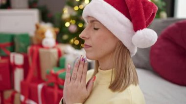 Genç sarışın kadın dua ediyor evde Noel ağacının yanında oturuyor