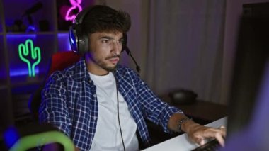 Yakışıklı genç bir Arap, kendine güvenen bir oyuncu, video oyununda geceyi kazanıyor, oyun odasında tezahürat yapıyor, ekranda ışıldayan muzaffer bir gülümseme.