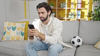 Genç İspanyol adam evde akıllı telefon kullanarak futbol maçı izliyor.