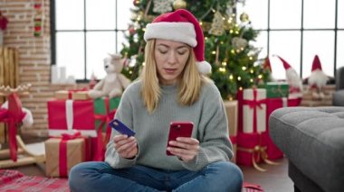 Akıllı telefon ve kredi kartı kullanan genç sarışın kadın Noel 'i evde kutluyor.
