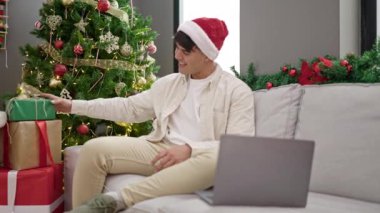 Genç İspanyol adam Noel hediyesini elinde tutarken görüntülü arama yapıyor.