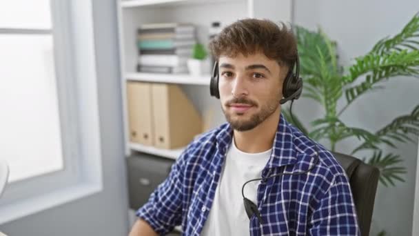 快乐的阿拉伯人 带着自信的笑容 在公司工作 给自己的办公空间增色不少 抱怨自己要戴耳机来帮助客户服务 — 图库视频影像