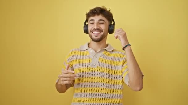 自信的年轻Arab男人呻吟着在耳机上的音乐 在孤独的黄墙前独自快乐地跳舞 散发着积极向上和幸福的光芒 — 图库视频影像