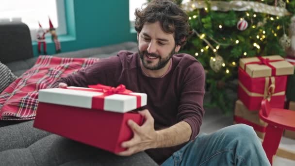 Jovem Hispânico Sorrindo Confiante Desempacotar Livro Presente Natal Casa — Vídeo de Stock
