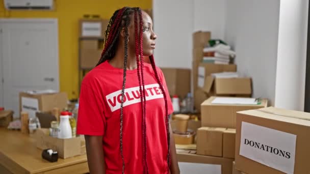 一位漂亮的非洲裔美国妇女 一位严肃的志愿者 站在慈善中心的仓库里 穿着T恤衫的成年工作者 站在挤满了人的捐赠物背后 以无私的精神团结在一起 — 图库视频影像