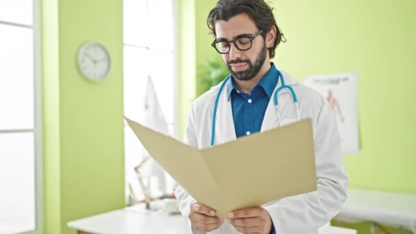 Νεαρός Ισπανός Γιατρός Διαβάζει Ιατρική Έκθεση Χαμογελώντας Στην Κλινική — Αρχείο Βίντεο