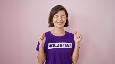 Genç, kendine güvenen İspanyol kadın gönüllü olarak zaferini kutluyor. Üniformalı bir tişört ve kısa saç stiliyle izole edilmiş pembe arka planda kahkahalar atıyor.