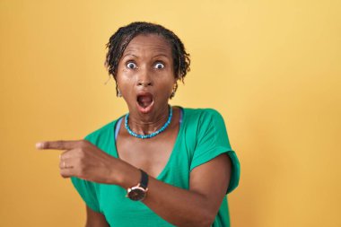 Sarı arka planda dikilen Afrikalı kadın parmağını yana çevirerek şaşırdı, ağzı açık hayret içinde kaldı.. 