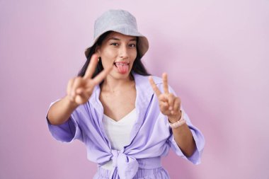 Pembe arka planda dikilen genç İspanyol kadın şapkasını takmış, ağzı açık gülümsüyor ve iki elini de zafer işareti yaparken gösteriyor. İki numara.. 