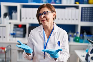 Middle age woman scientist smiling confident speaking at laboratory