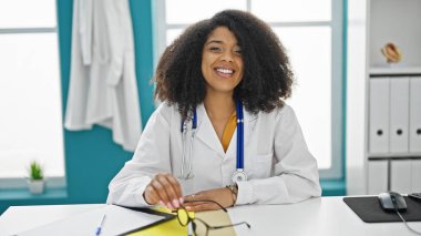 Afrikalı Amerikalı kadın doktor, klinikteki masada kendinden emin bir şekilde oturuyor.