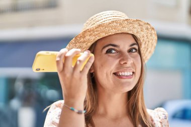 Yaz şapkası takan genç bir turist sokakta akıllı telefondan sesli mesaj dinliyor.