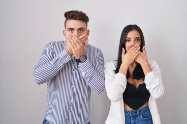 Young hispanic couple standing over white background shocked covering mouth with hands for mistake. secret concept. 