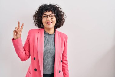 Kıvırcık saçlı İspanyol kadın izole edilmiş arka planda duruyor. İki numaralı parmaklarıyla işaret ediyor ve gülümsüyor. Kendinden emin ve mutlu.. 