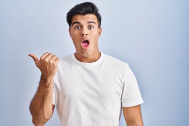 Mavi arka planda dikilen İspanyol adam, elleri yana doğru işaret ederek şaşırdı, ağzı açık hayret içinde kaldı.. 