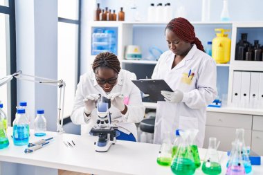 Afrikalı Amerikalı kadın bilim adamları laboratuardaki belgelerde mikroskop kullanıyorlar.