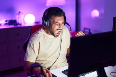 Oyun odasında İspanyol asıllı genç adam video oyunu oynuyor.