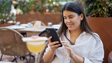 Genç ve güzel İspanyol kadın akıllı telefon kullanıyor. Bar terasında masada oturuyor.