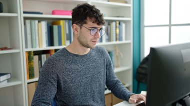Young hispanic man student using computer studying at library university