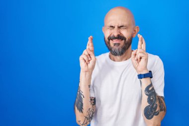 Mavi arka planda dikilen İspanyol dövmeli adam umut ve gözleriyle gülümseyerek işaret ediyor. Şans ve batıl inançlar. 