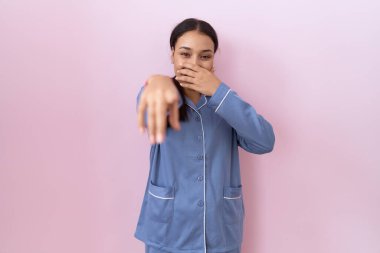 Mavi pijama giyen genç Arap kadın sana gülüyor, eli ağzında kamerayı işaret ediyor, utanç ifadesi. 