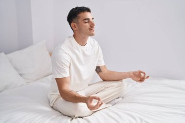 Young hispanic man doing yoga exercise sitting on bed at bedroom