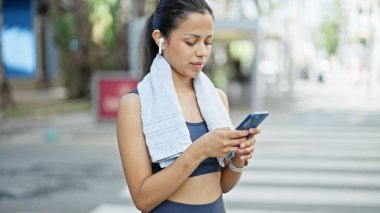 Young beautiful hispanic woman wearing sportswear using smartphone at street