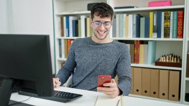 Kütüphanede akıllı telefon kullanan genç İspanyol öğrenci.