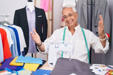 Gri saç terzisi dikiş makinesi kullanan orta yaşlı bir adam kameraya bakıp sarılmak için gülümsüyor. Mutluluğu kucaklayan neşeli bir ifade.. 