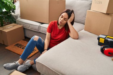 Young beautiful hispanic woman sitting on floor with tired expression at new home