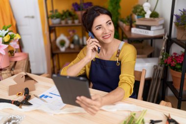Çiçekçide dokunmatik ped kullanan orta yaşlı İspanyol çiçekçi kadın.