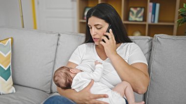 Anne ve bebek kanepede oturup emziriyorlar ve evde telefonla konuşuyorlar.