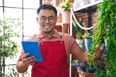 Young chinese man florist smiling confident using touchpad at florist