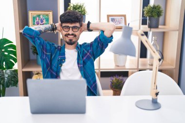 Young hispanic man using laptop relaxed with hands on head at home