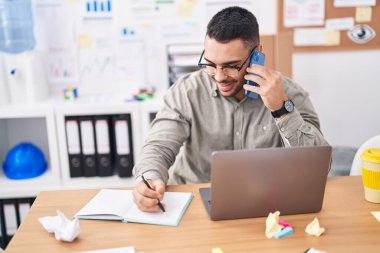 Genç İspanyol iş adamı akıllı telefondan konuşuyor. Ofisteki defterde yazıyor.