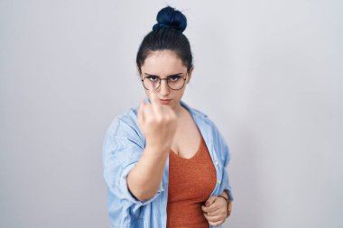 Young modern girl with blue hair standing over white background showing middle finger, impolite and rude fuck off expression 