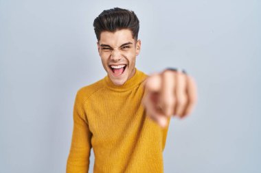 Mavi arka planda dikilen Latin asıllı genç adam kameraya kızgın ve sinirli olduğunu gösteriyor. 