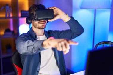 Oyun odasında sanal gerçeklik gözlüğü kullanarak video oyunu oynayan beyaz bir genç adam.