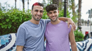 Two men couple smiling confident hugging each other at park
