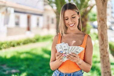 Young beautiful hispanic woman smiling confident counting dollars at park