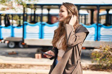 Parkta akıllı telefon kullanarak gülümseyen güzel bir İspanyol kadın.