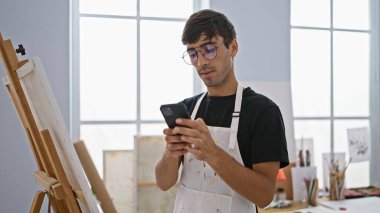 Yakışıklı genç İspanyol ressam, resim stüdyosunun göbeğinde fırçalar ve tuvaller arasında akıllı telefonlara yoğunlaşarak kendini yaratıcılığa kaptırdı.