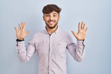 Mavi arka planda duran sakallı bir Arap on numarayı gösterip işaret ederken kendinden emin ve mutlu gülümsüyor.. 