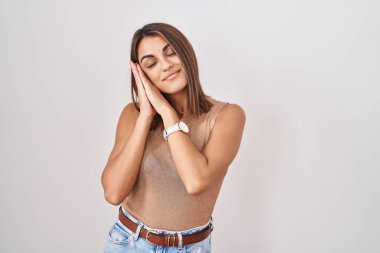 Young hispanic woman standing over white background sleeping tired dreaming and posing with hands together while smiling with closed eyes. 