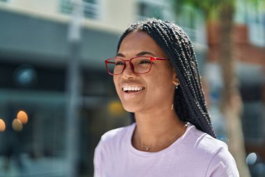 Sokakta kendine güvenen gözlüklü, gülümseyen Afrikalı Amerikalı kadın.