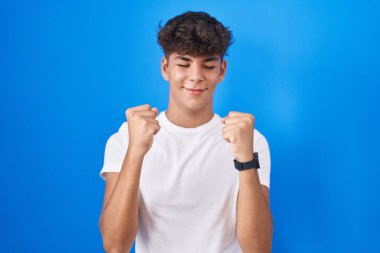 Mavi arka planda duran İspanyol ergen kolları havada ve gözleri kapalı gülümseyerek zaferi kutluyor. Kazanan konsept. 